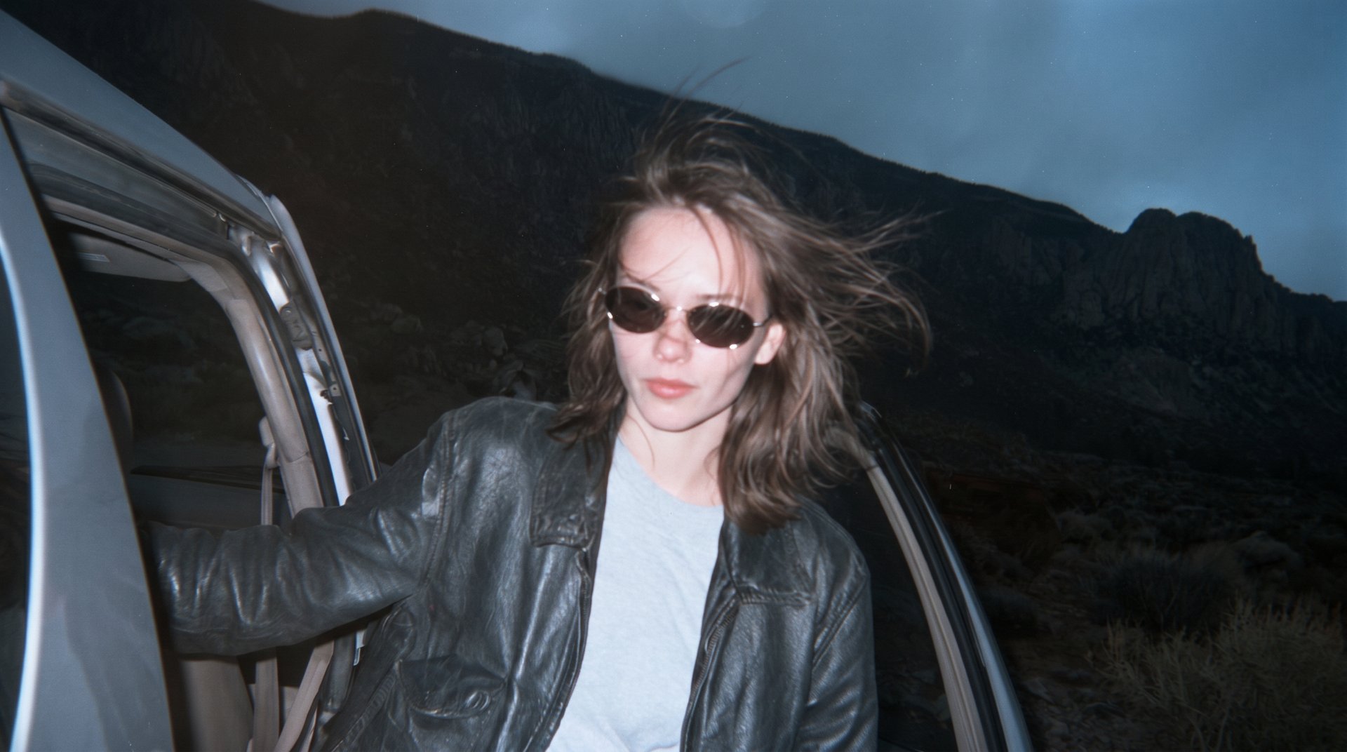 Retrato cándido con flash: una chica con gafas de sol junto a un coche, de noche